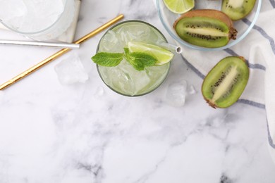 Photo of Glass of refreshing drink with lime and cut kiwi on white marble table, flat lay. Space for text