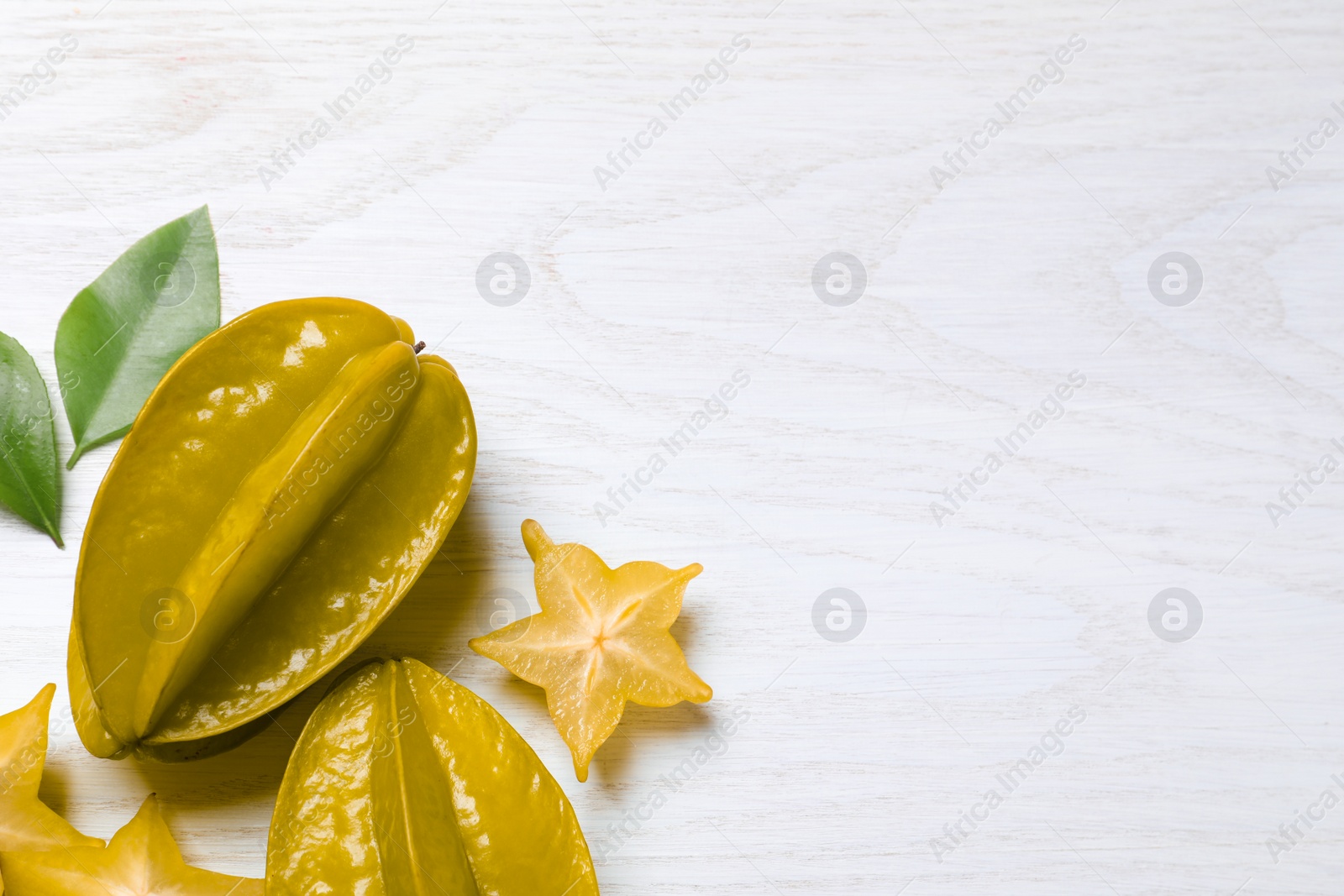 Photo of Delicious carambola fruits on white wooden table, flat lay. Space for text