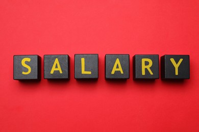 Image of Word Salary made with black wooden cubes on red background, flat lay