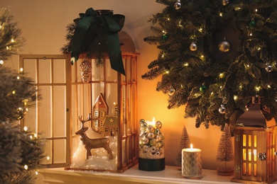 Photo of Beautiful wooden lanterns, festive wreath and other decorations on shelf in room with Christmas tree