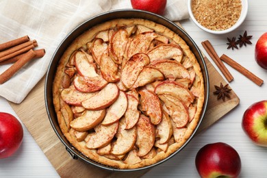 Delicious apple pie and ingredients on white wooden table, flat lay