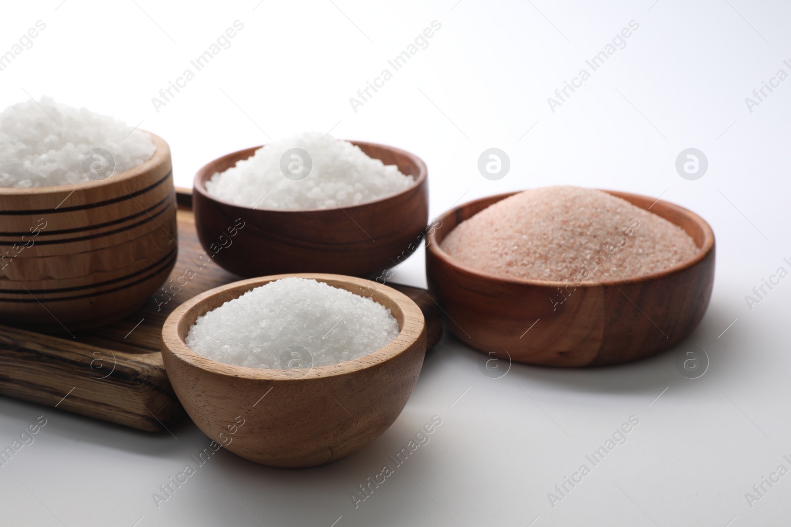 Photo of Different types of natural salt in wooden bowls on white background