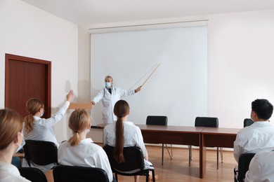 Photo of Senior doctor giving lecture near projection screen in conference room