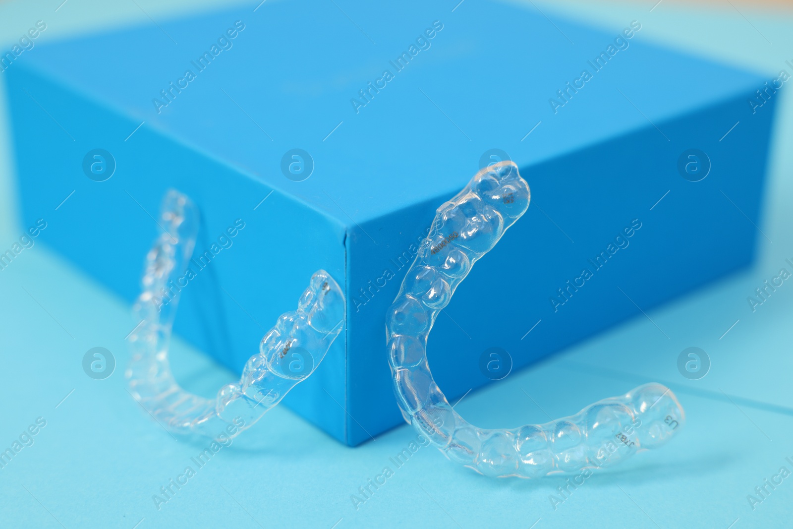 Photo of Transparent dental aligners on light blue background, closeup