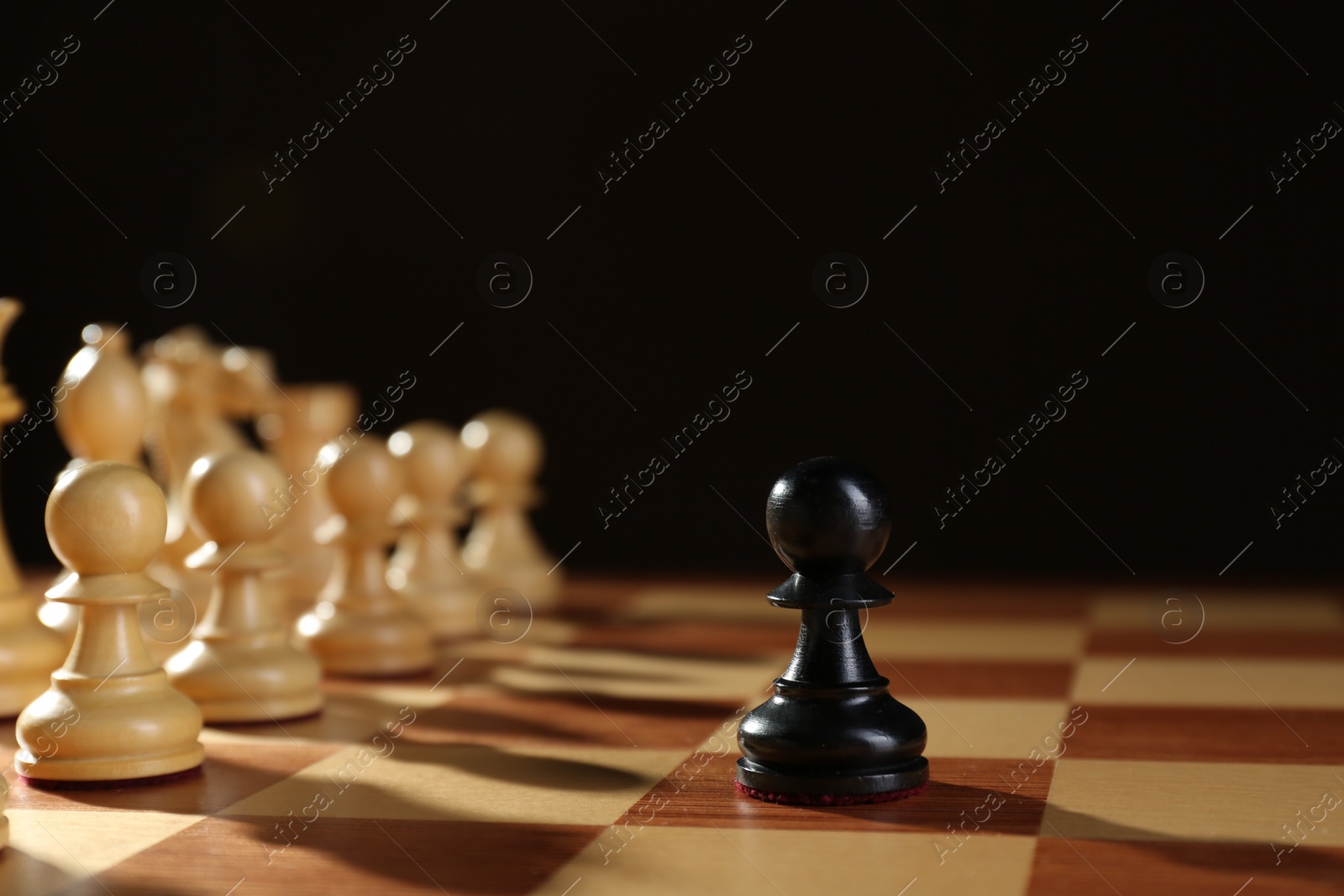 Photo of Black pawn in front of white pieces on wooden board against dark background. Competition concept