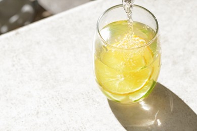 Photo of Pouring water into glass with lemon slices at light grey table, closeup. Space for text