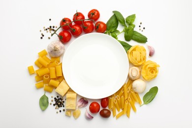 Photo of Plate surrounded by different types of pasta, products and peppercorns on white background, flat lay. Space for text