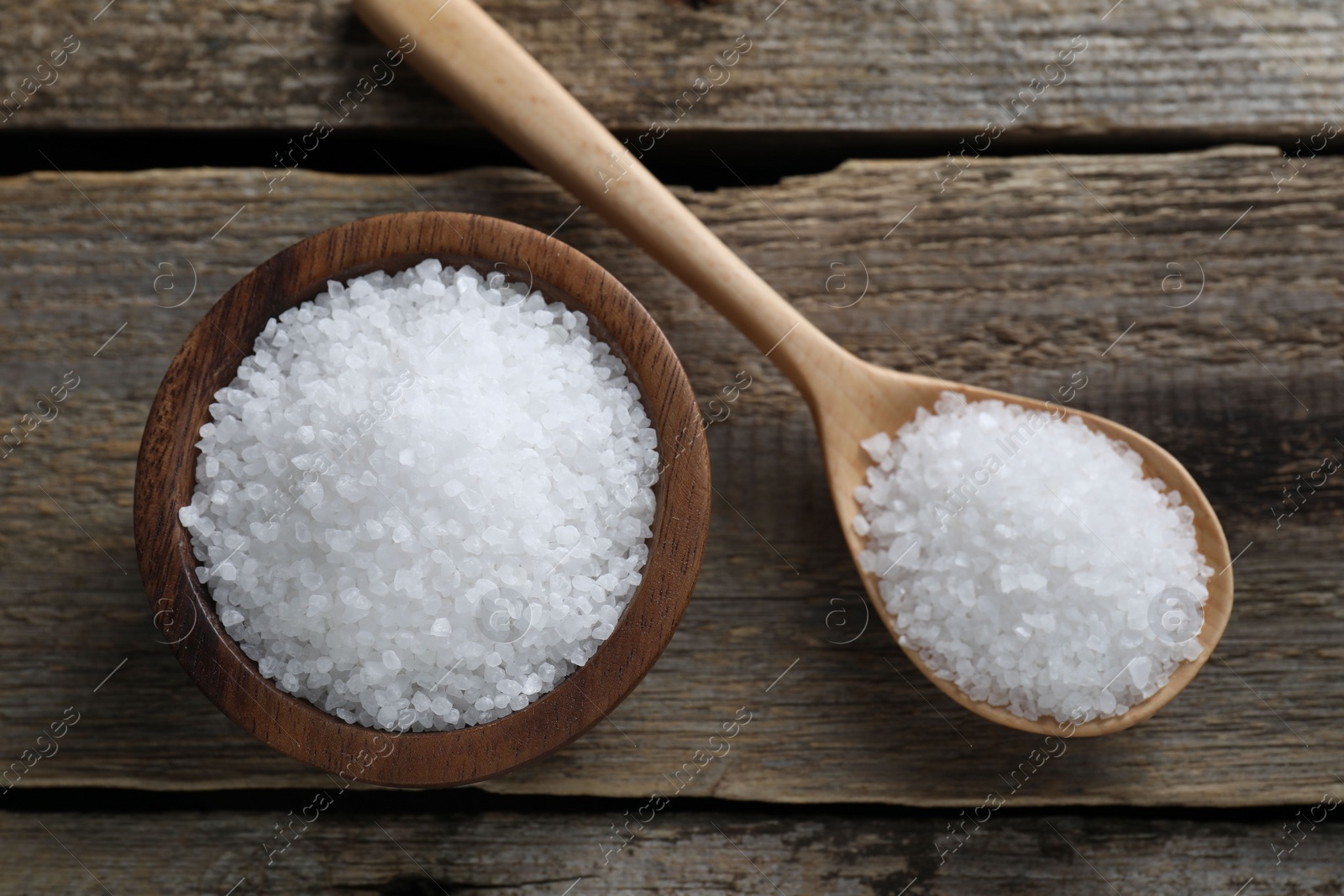 Photo of Organic salt in bowl and spoon on wooden table, flat lay