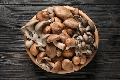 Photo of Different fresh wild mushrooms in bowl on wooden background, top view