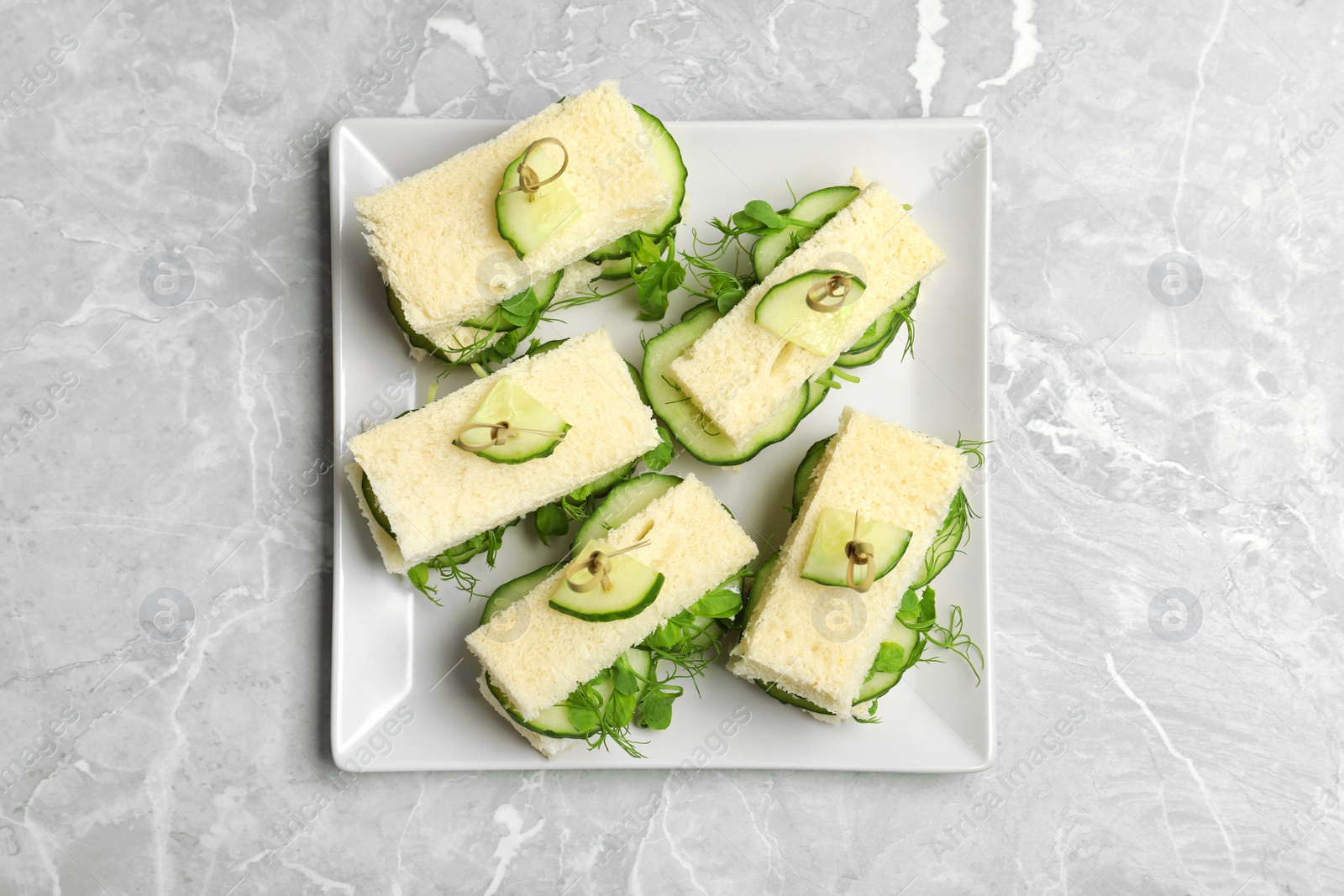 Photo of Plate with traditional English cucumber sandwiches on grey background, top view