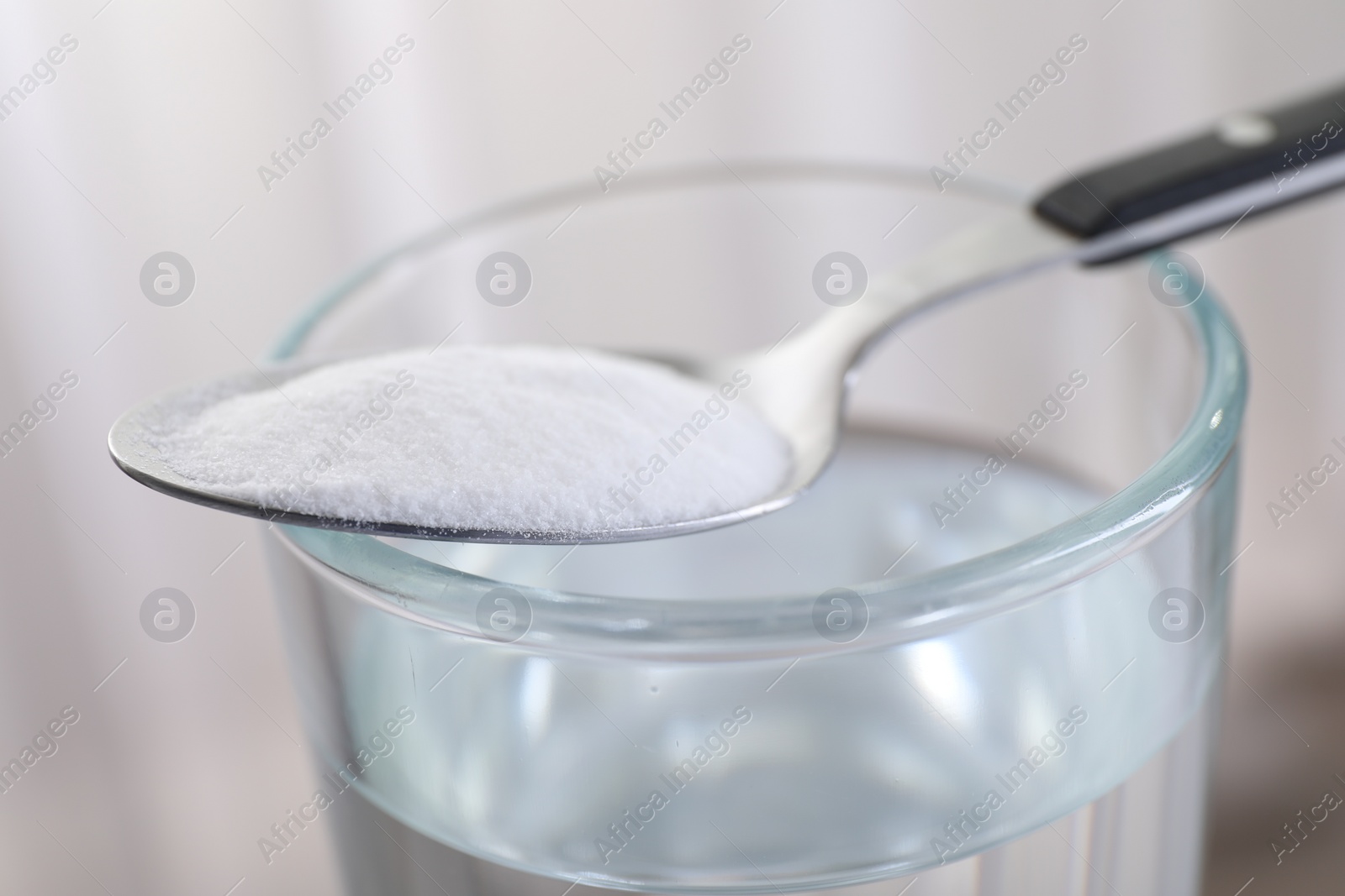 Photo of Glass of water and spoon with baking soda on light background, closeup