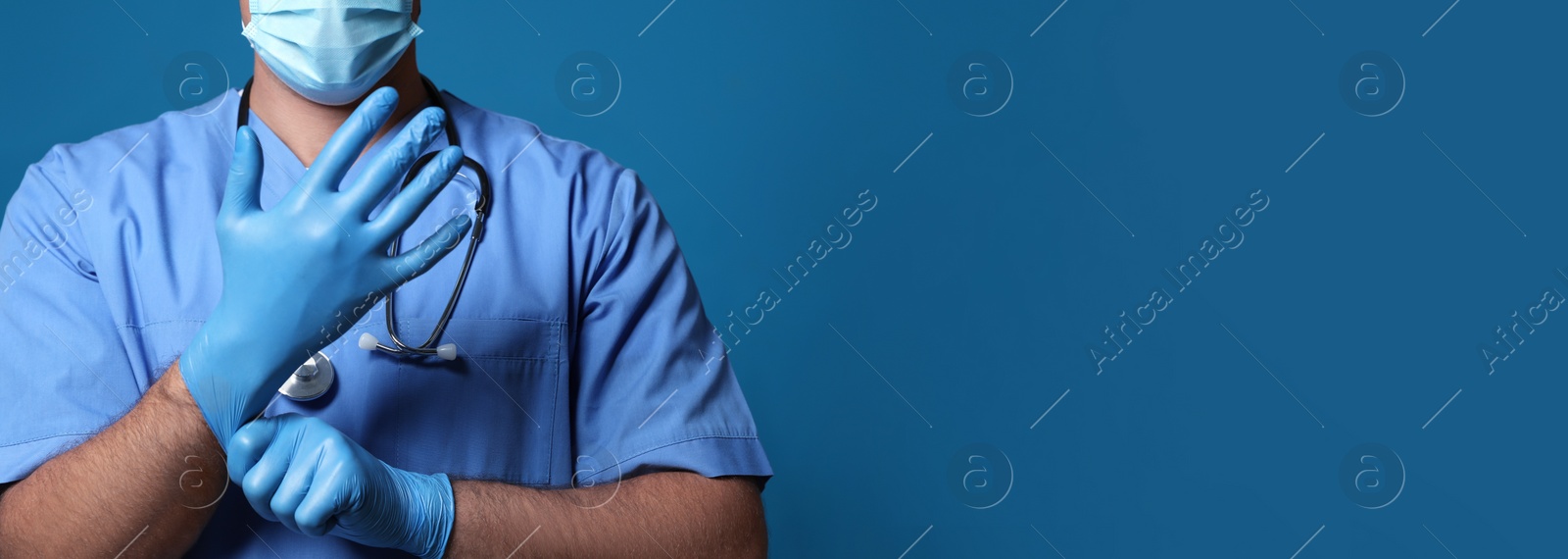 Image of Surgeon putting on medical gloves against blue background, closeup. Banner design with space for text