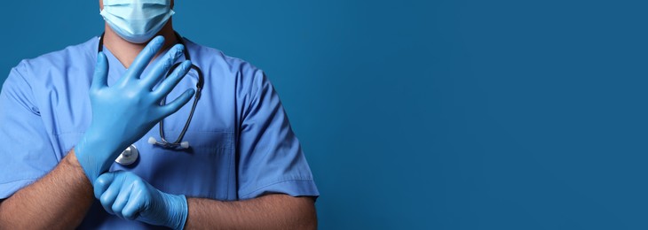 Surgeon putting on medical gloves against blue background, closeup. Banner design with space for text