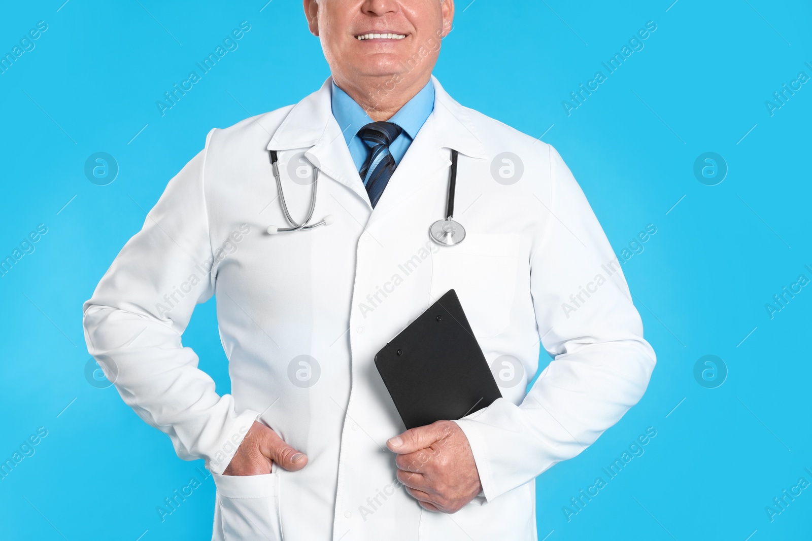Photo of Senior doctor with clipboard on light blue background, closeup