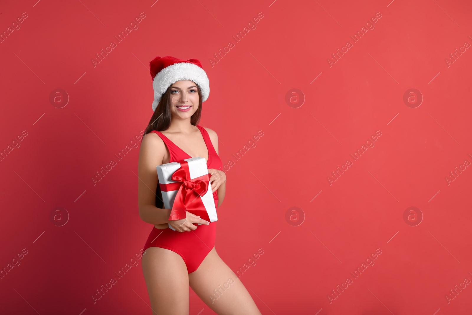 Photo of Young beautiful woman in swimsuit and Santa hat holding gift box on color background. Christmas celebration