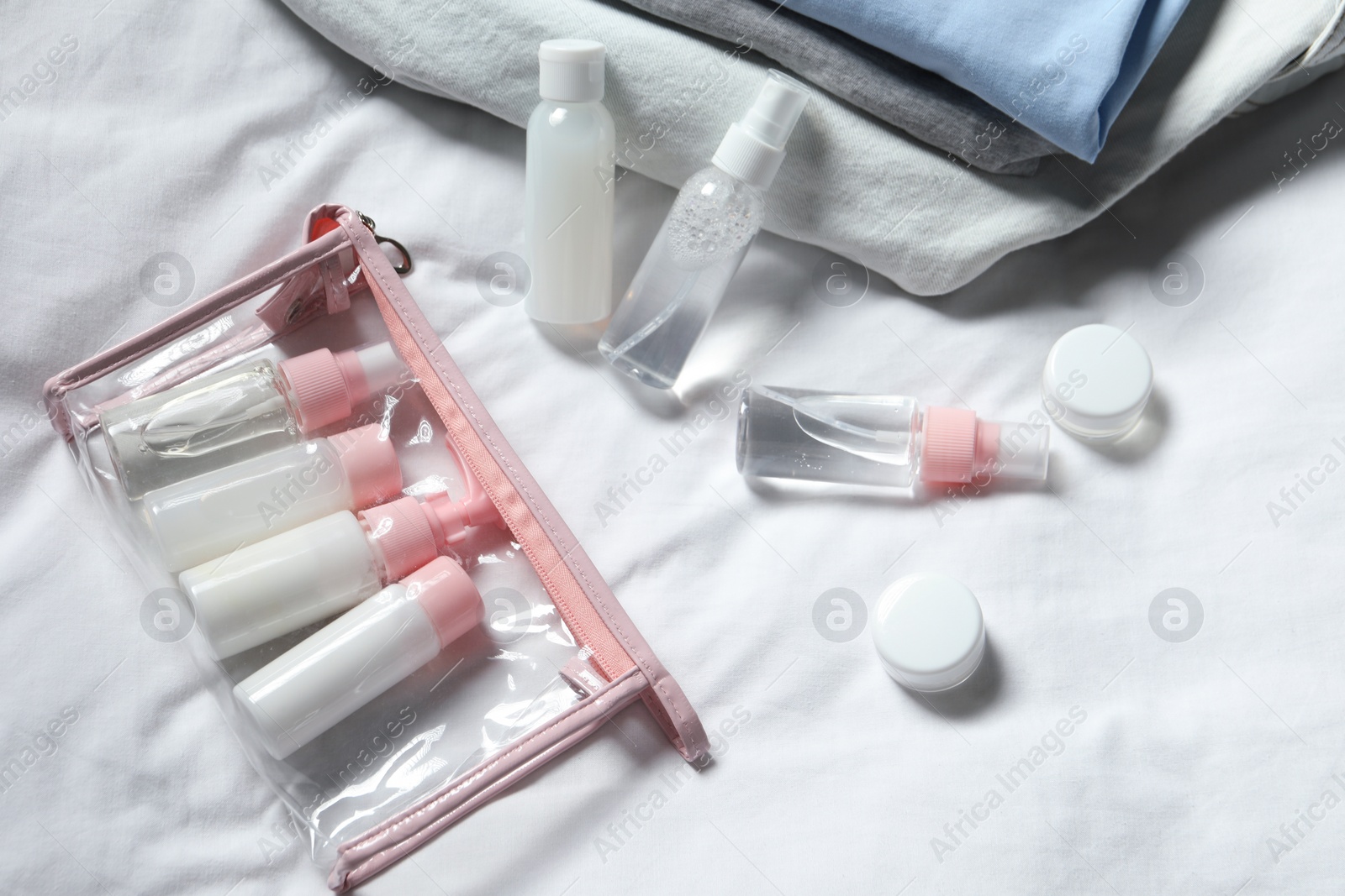 Photo of Cosmetic travel kit. Plastic bag with small containers of personal care products on bed