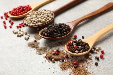 Photo of Aromatic spice. Different peppers in spoons on light textured table, closeup