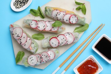 Delicious spring rolls served on light blue background, flat lay