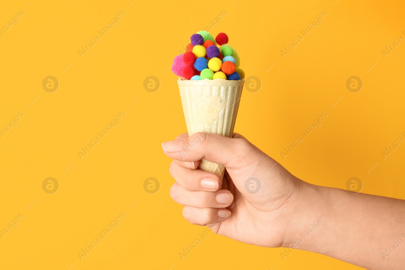 Photo of Woman holding ice cream waffle with fluffy balls on yellow background, closeup