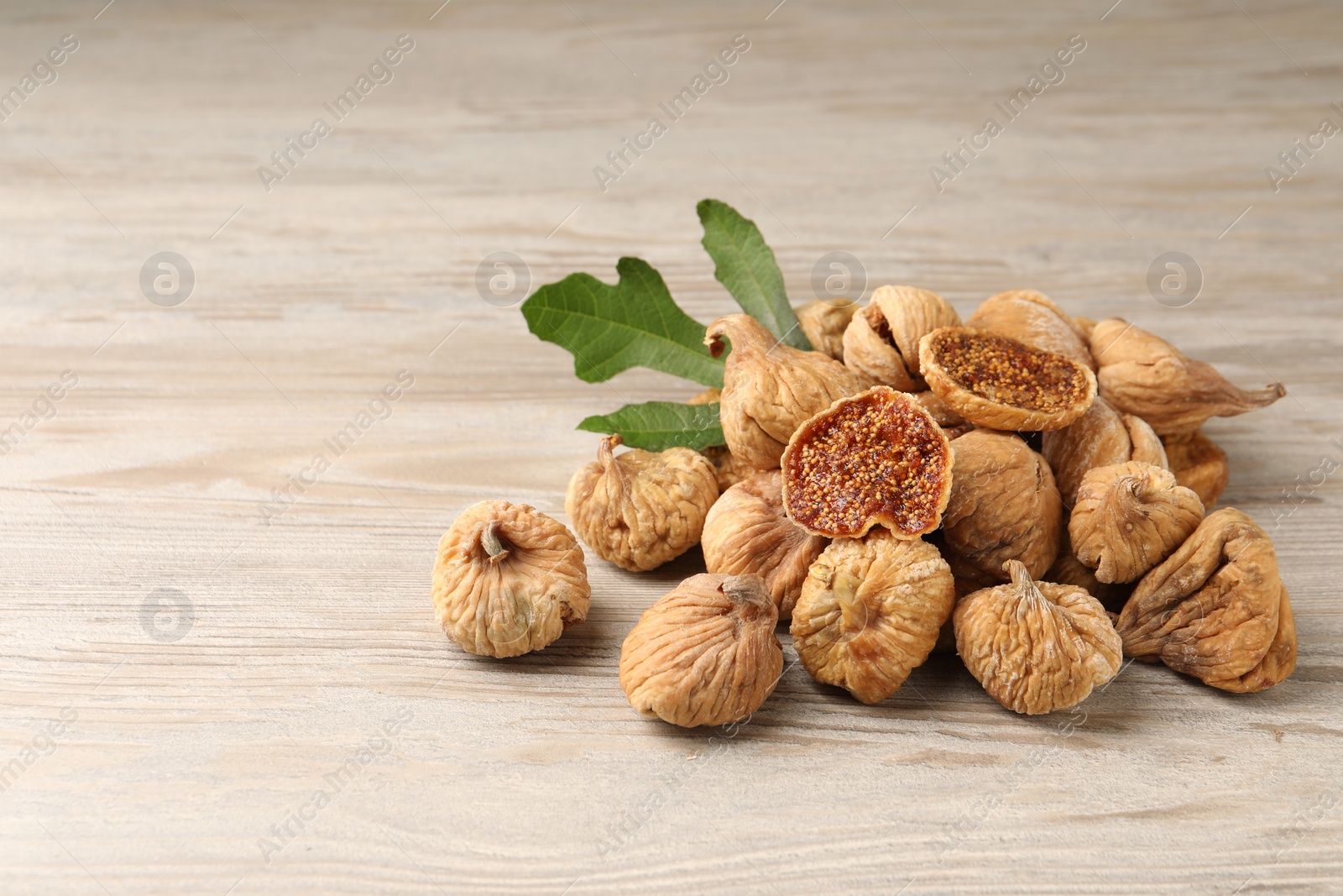 Photo of Tasty dried figs and green leaf on light wooden table. Space for text