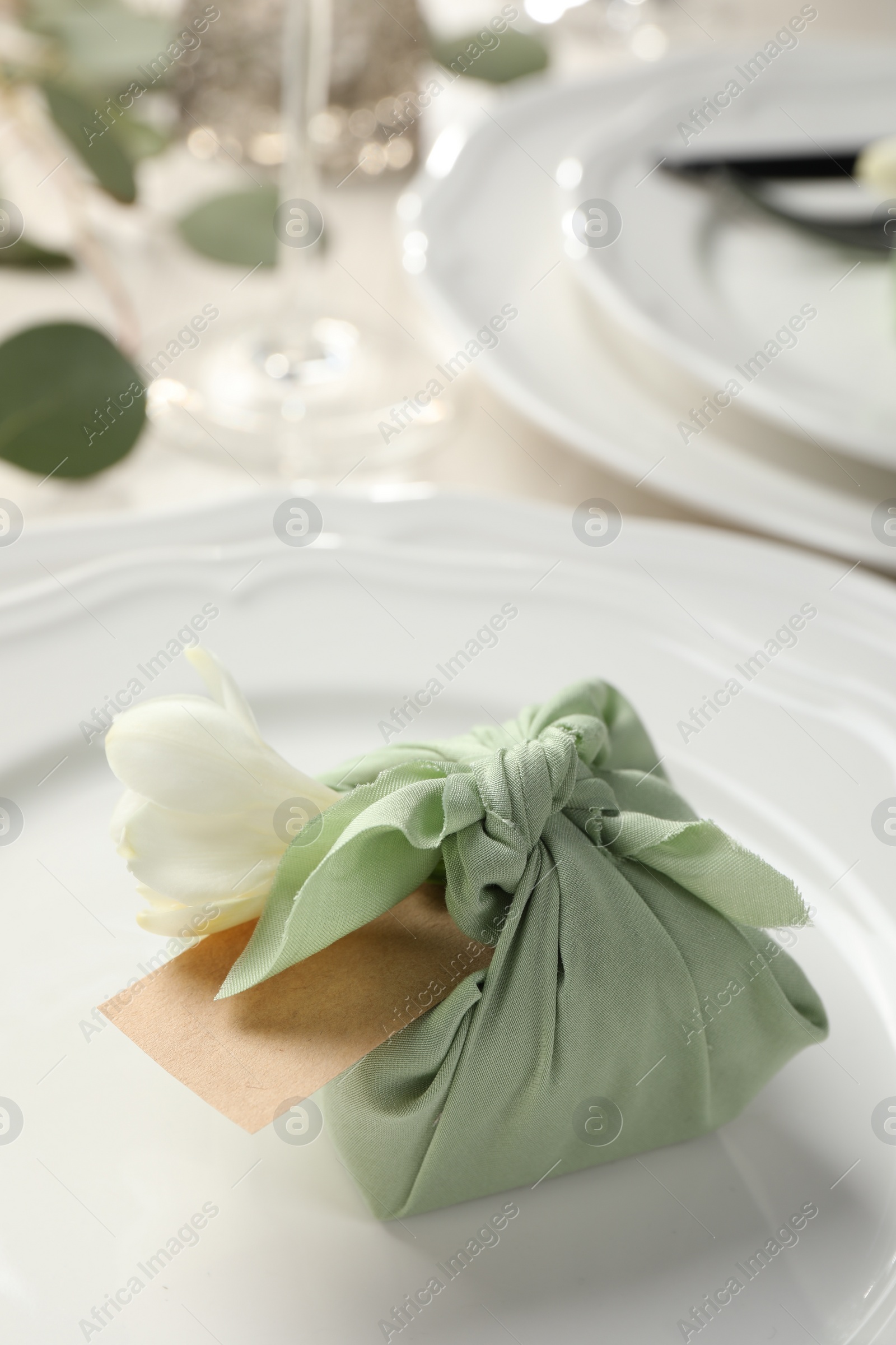 Photo of Furoshiki technique. Gift packed in green fabric with flower and blank card on table, closeup