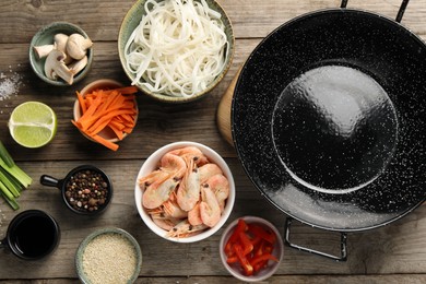 Flat lay composition with black wok, spices and products on wooden table