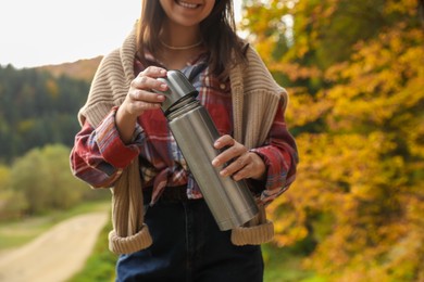 Photo of Woman with metallic thermos in mountains, closeup