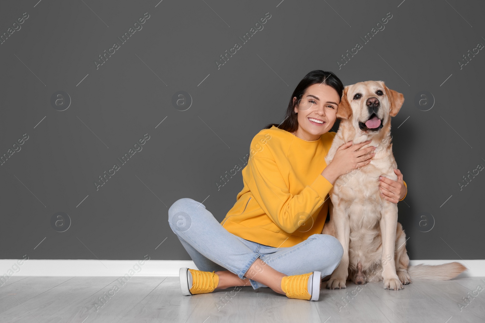 Photo of Happy woman with cute Labrador Retriever on floor against grey wall