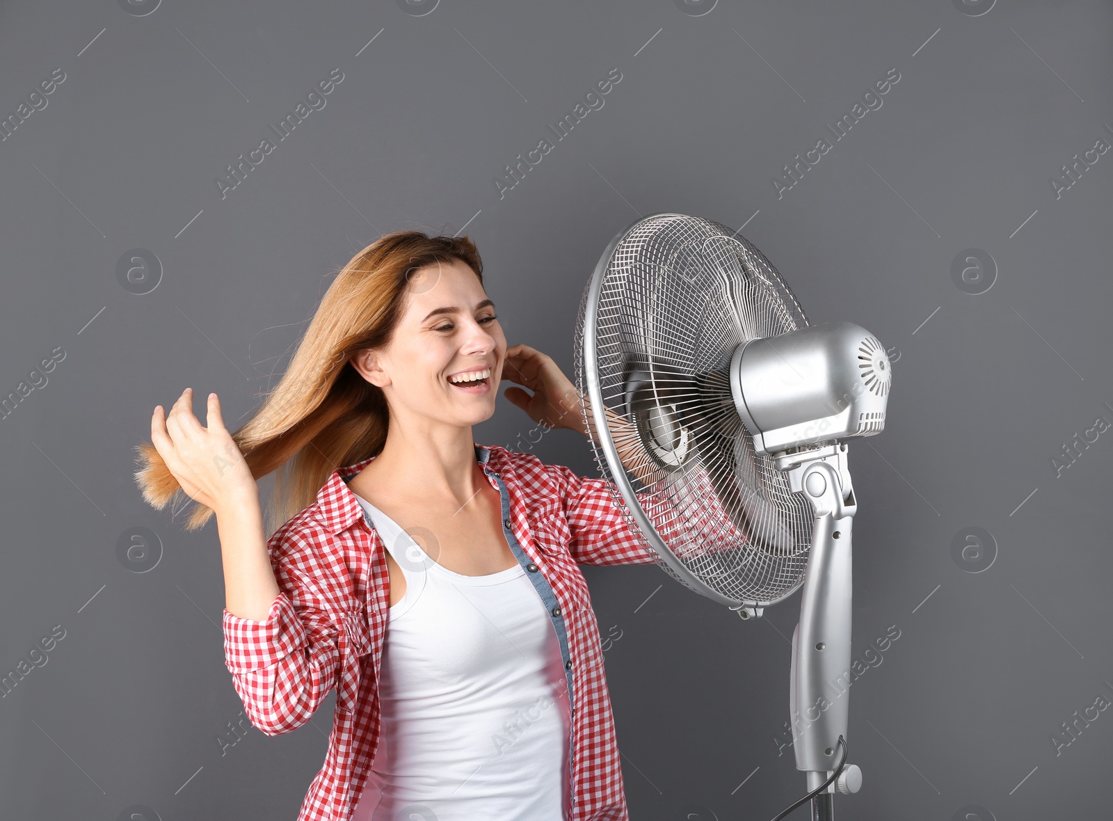 Photo of Woman refreshing from heat in front of fan on grey background