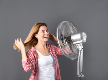 Woman refreshing from heat in front of fan on grey background