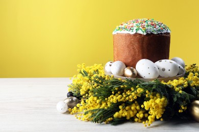 Traditional Easter cake with sprinkles, painted eggs and beautiful spring flowers on white wooden table, space for text