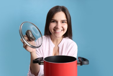 Happy young woman with cooking pot on light blue background