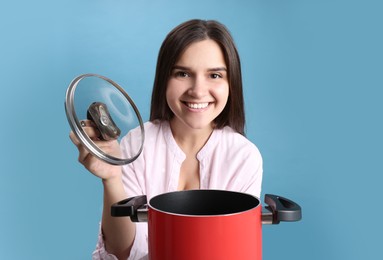 Photo of Happy young woman with cooking pot on light blue background