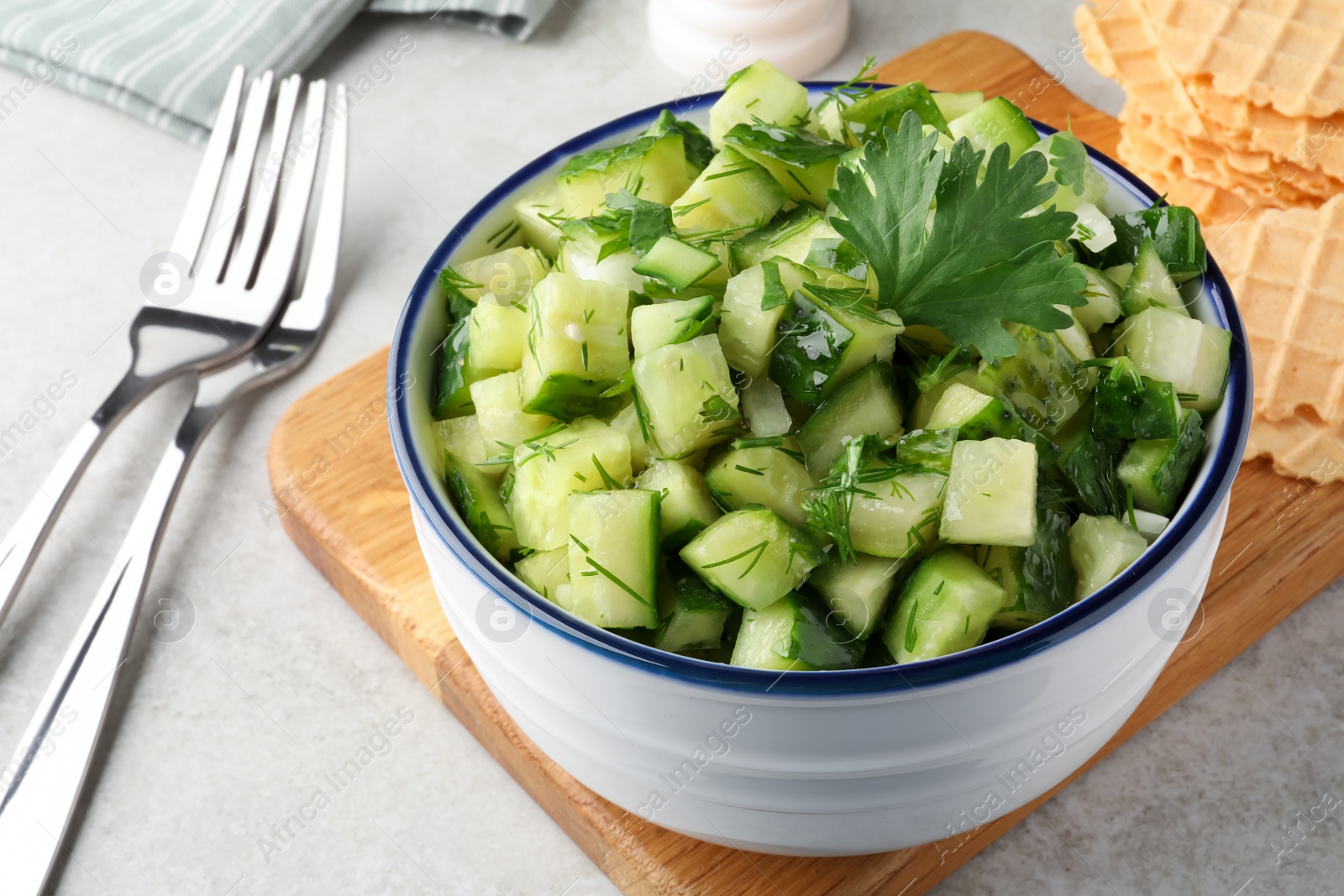 Photo of Bowl of delicious cucumber salad served on light table, closeup