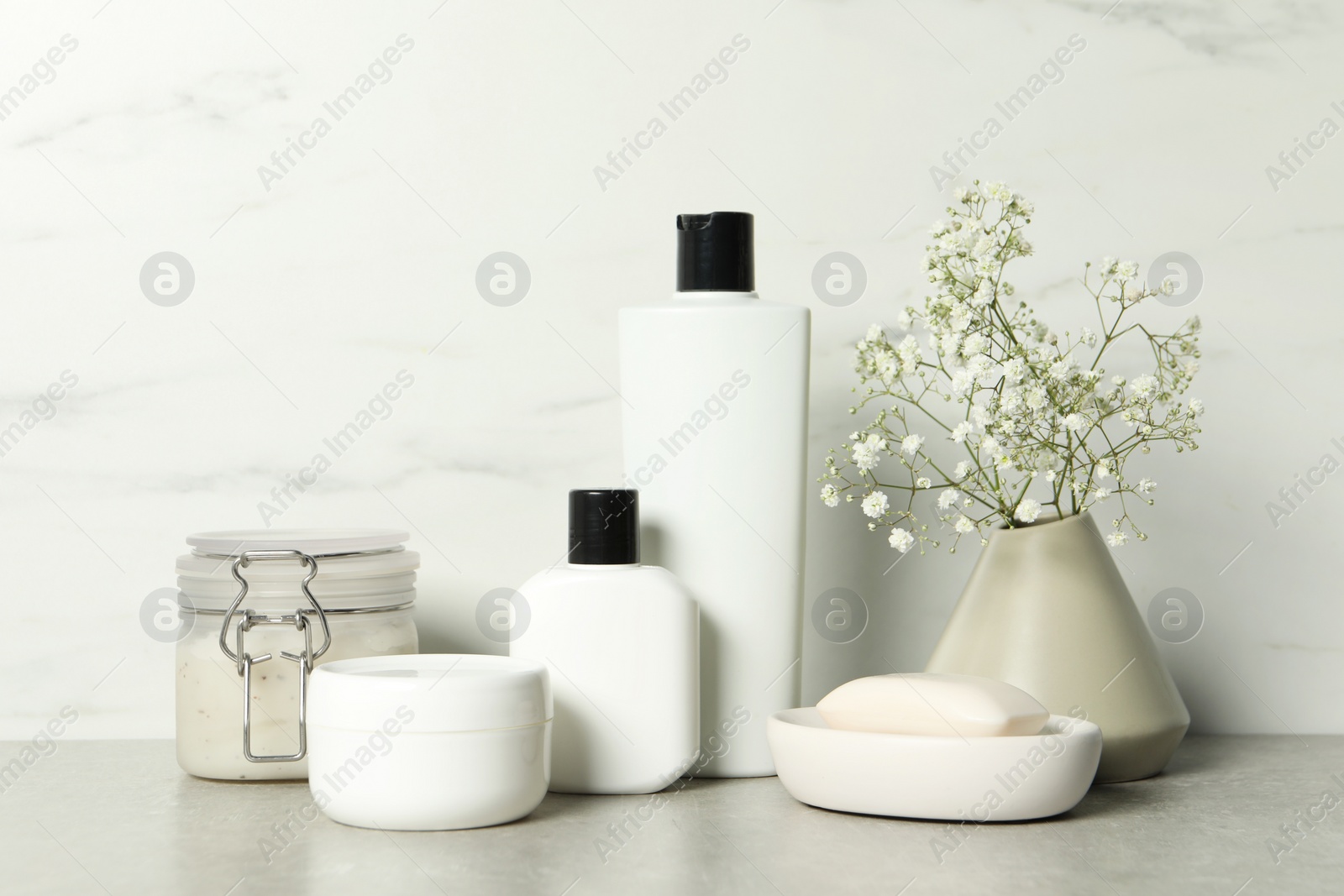 Photo of Bath accessories. Personal care products and gypsophila flowers in vase on gray table near white marble wall