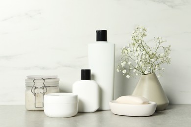 Bath accessories. Personal care products and gypsophila flowers in vase on gray table near white marble wall