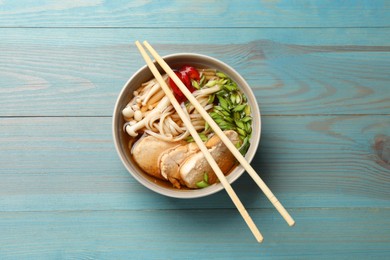 Photo of Delicious ramen with meat in bowl and chopsticks on light blue wooden table, top view. Noodle soup