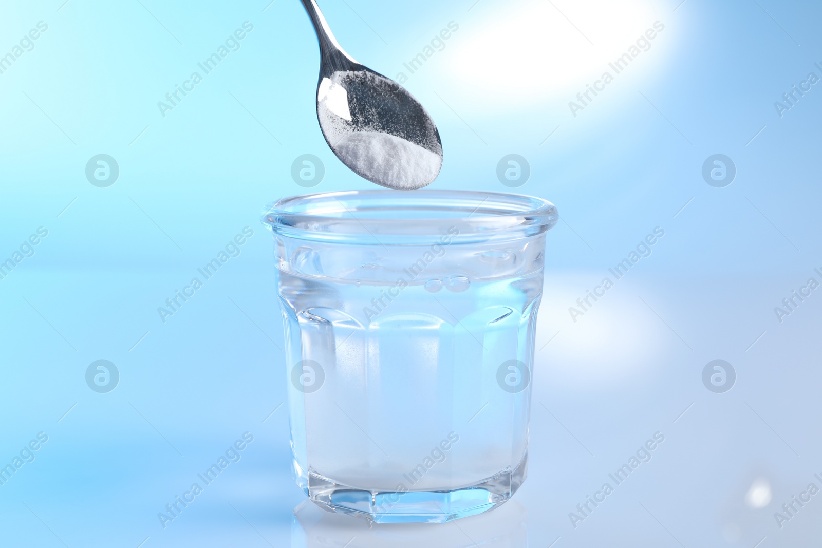 Photo of Adding baking soda into glass of water on light blue background