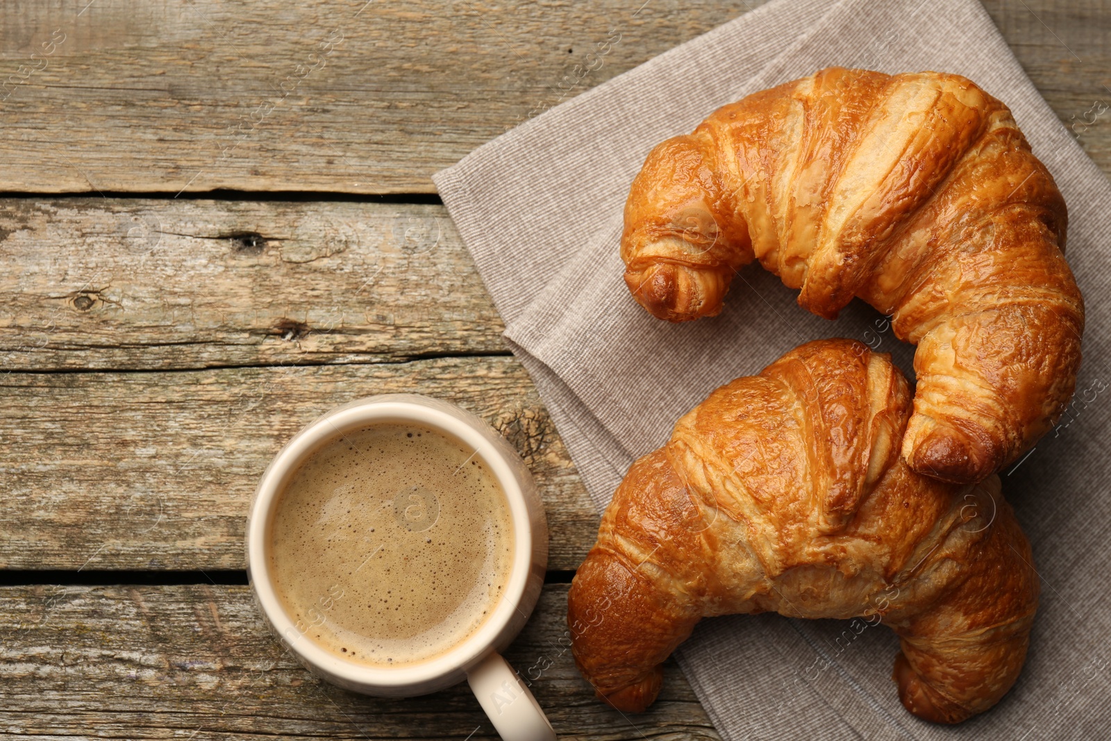 Photo of Delicious fresh croissants and cup of coffee on wooden table, flat lay