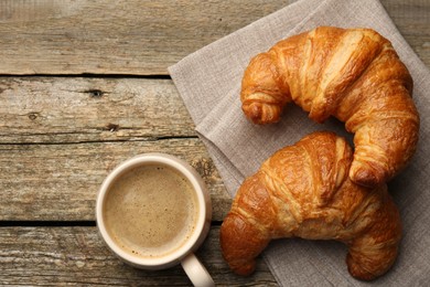 Delicious fresh croissants and cup of coffee on wooden table, flat lay