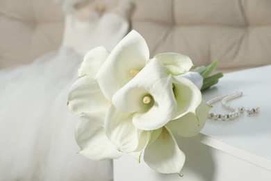 Beautiful calla lily flowers tied with ribbon and jewelry on white chest of drawers indoors