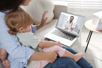 Image of Mother and daughter having online consultation with pediatrician via laptop on sofa at home