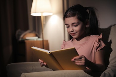 Photo of Little girl reading fairy tale at home in evening