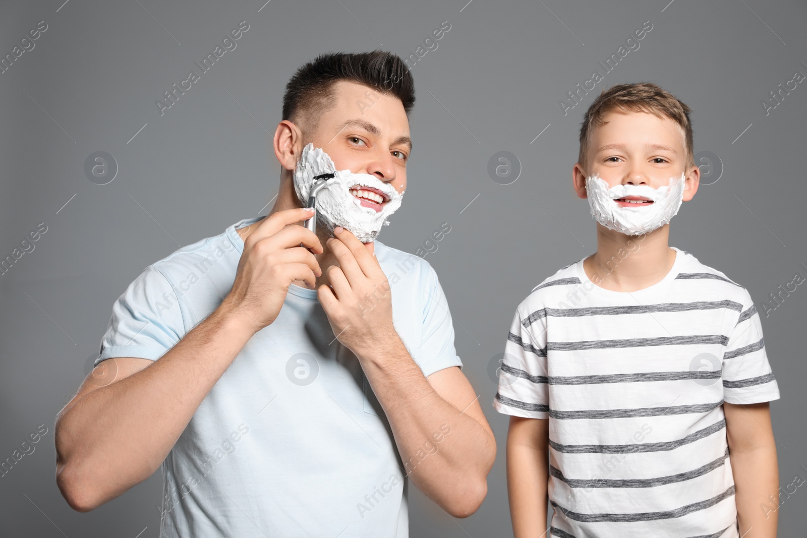 Photo of Dad and son with shaving foam on faces, grey background