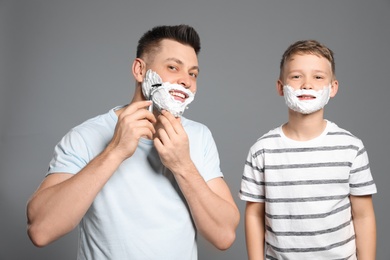 Photo of Dad and son with shaving foam on faces, grey background