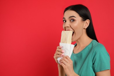 Young woman eating delicious shawarma on red background. Space for text