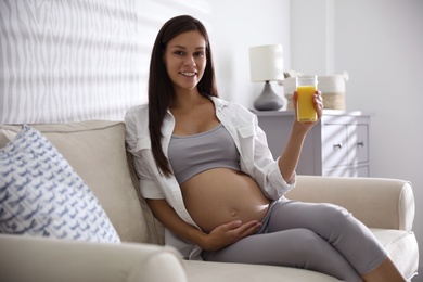 Photo of Young pregnant woman with glass of juice in living room. Taking care of baby health