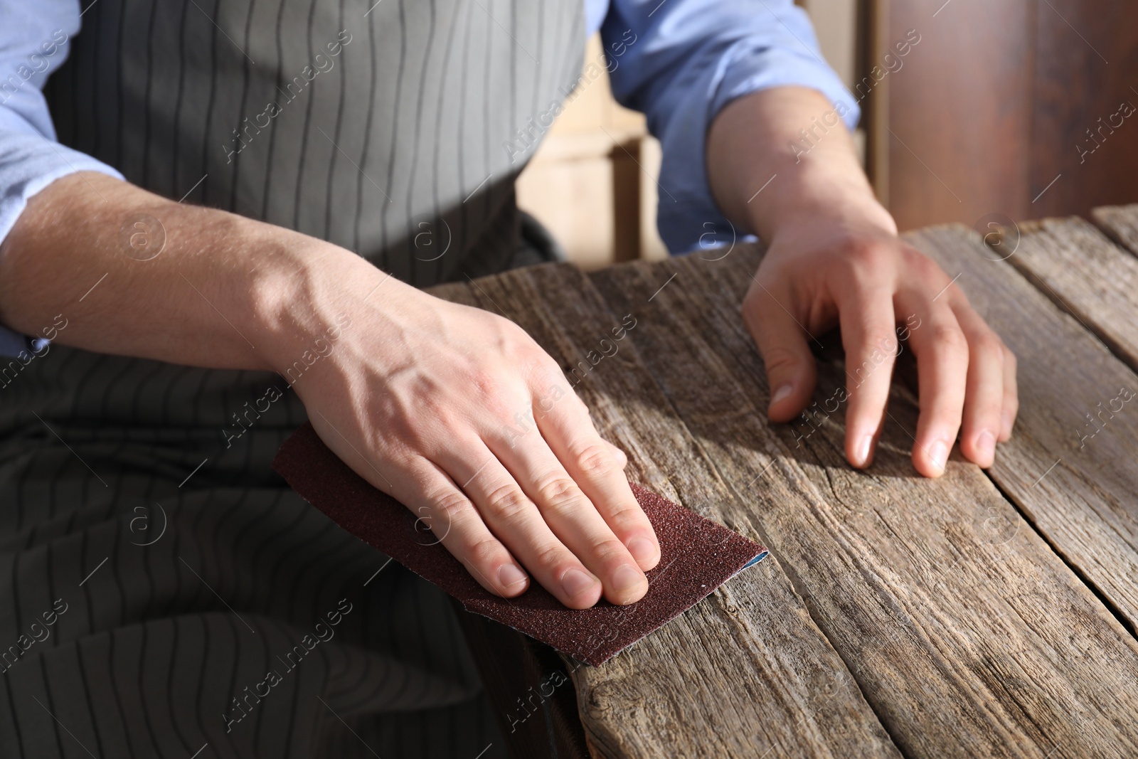 Photo of Man polishing wooden table with sandpaper indoors, closeup