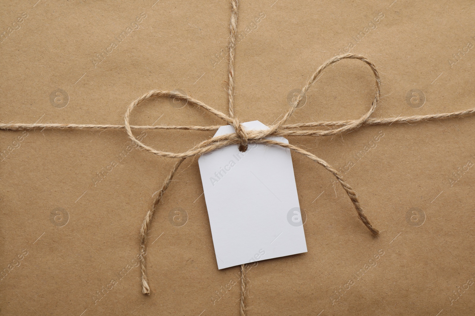 Photo of Parcel wrapped in kraft paper with tag as background, closeup