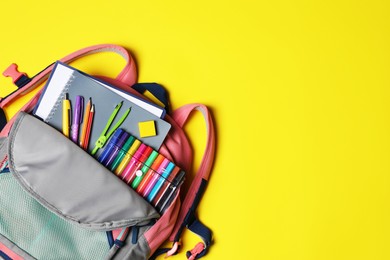 Photo of Backpack with school stationery on yellow background, top view. Space for text